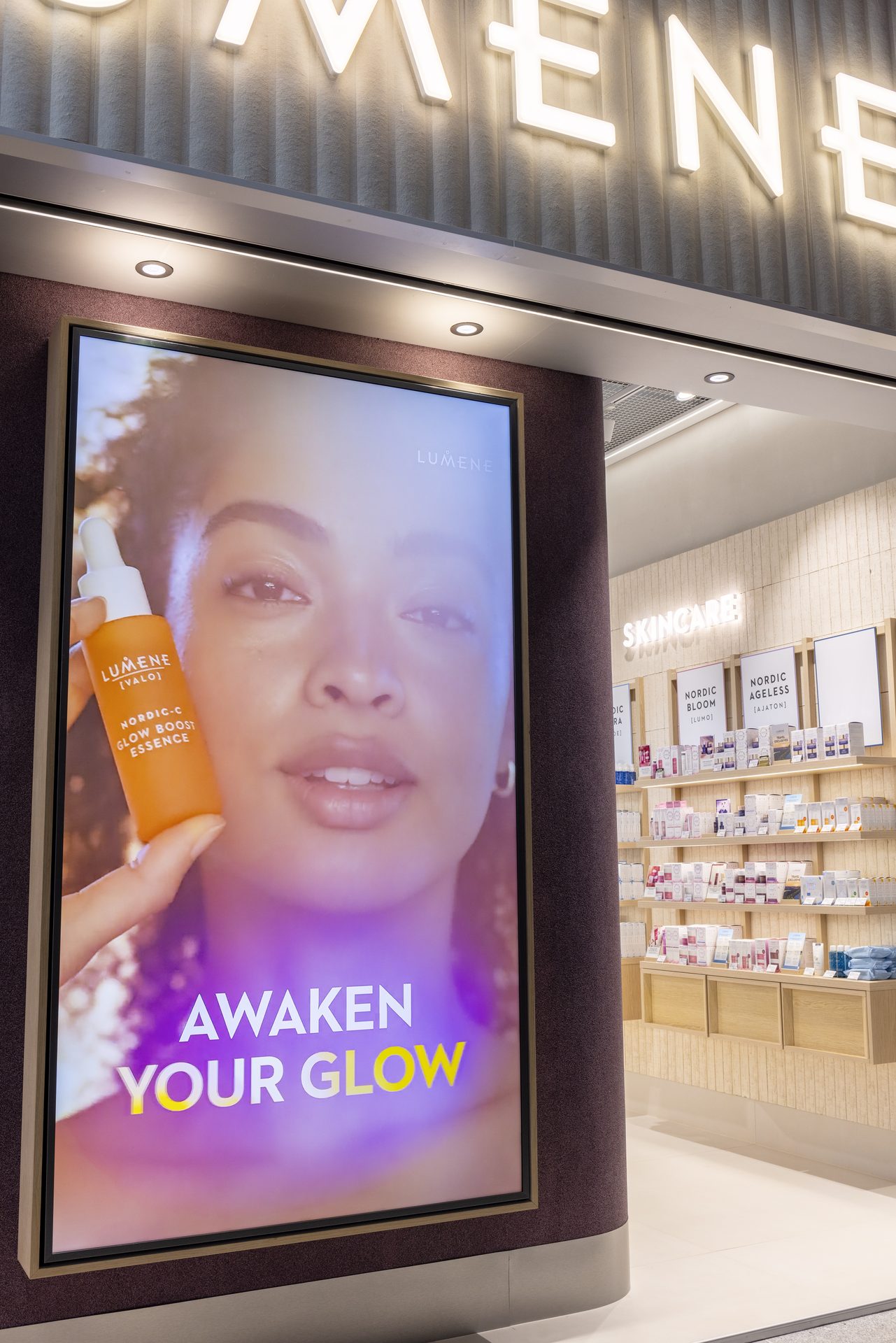 Large vertical digital screen beside a Lumene skincare wall