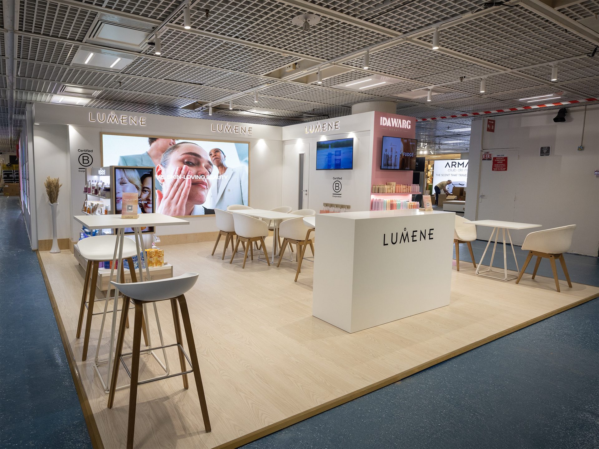 Lumene trade-fair booth lounge with a large LED wall and white cafe seating